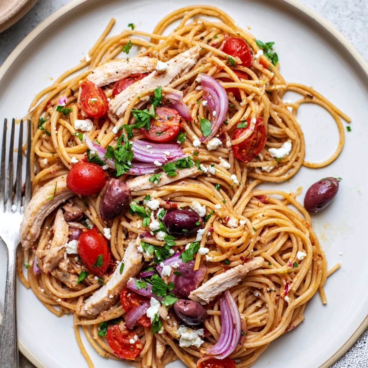 Griechische Hühnchen-Spaghetti auf einem hellen Teller mit gegrilltem Hühnchen, Kirschtomaten und Feta.