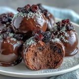 Ein Löffel voll schwarzer Johannisbeerganache wird in geschmolzene dunkle Schokolade getaucht und tropft sanft auf das Backblech.