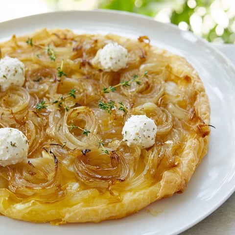 Golden, flaky Tarte Fine with Onions & Thyme, showcasing a rustic French appetizer ready to be sliced.