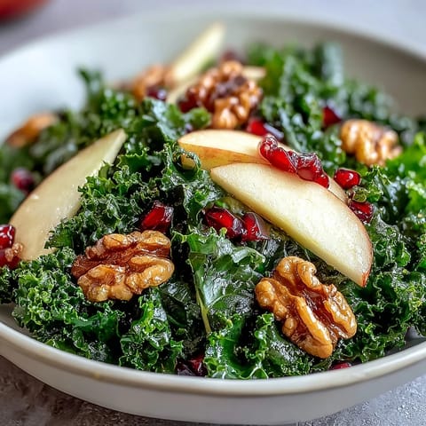 Vibrant Kale and Pomegranate Bowl topped with chopped walnuts and sliced apples, dressed in a light vinaigrette.  