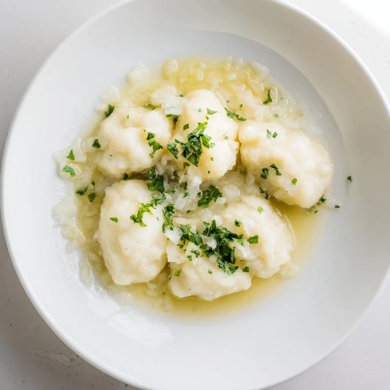 Close-up of fluffy Kartoffelklöße, drizzled with savory sauce, ready to be served with butter.